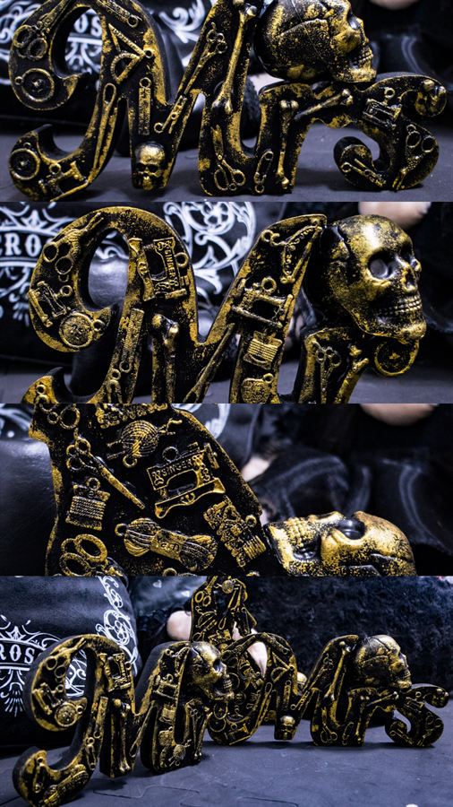 Schriftzug mit Nähwerkzeug-Reliefs und Totenkopf in Schwarz-Gold